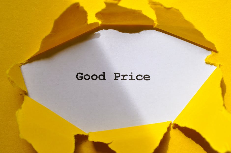 A close-up view of a bright yellow paper background with a tear in the center, revealing a white paper underneath that displays the words 'Good Price' in black, typewriter-style font. The torn yellow paper has irregular, jagged edges and some curled sections, suggesting it was torn manually. The image's lighting is even, with some shadows created by the torn edges, emphasizing the three-dimensional quality of the paper layers. The overall composition draws attention to the message 'Good Price', with the yellow background providing a vibrant contrast to the white inner paper. The scene appears to be a staged presentation possibly related to promotional or advertising content, with a clean, professional look suitable for illustrating affordable or value-based offerings, such as waste or rubbish removal services that emphasize cost-effectiveness and transparent pricing.